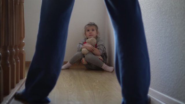 Scared child. Father and daughter. Child abuse concept. Child on the floor with teddy bear. 