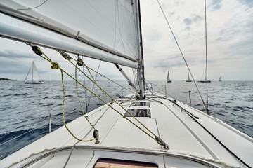 Croatia, Adriatic Sea, 19 September 2019: The race of sailboats, the team sits on the edge of a boat board, bright colors, view of participants of race from other boat through ropes and sails
