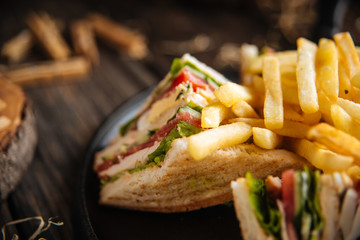 Closeup on sandwiches with fries on the black pan on the wooden table, horizontal format