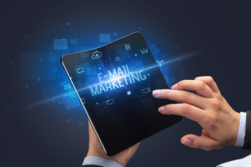 Businessman holding a foldable smartphone with E-MAIL MARKETING inscription, cyber security concept