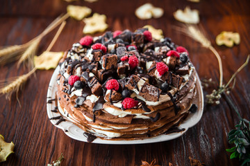 Appetizing sweet chocolate pancake cake decorated with berries on a wooden table, horizontal format