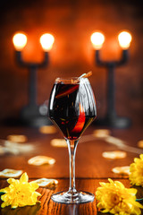 Side view on the delicious sweet red alcohol cocktail with cinnamon in wine glass on the wooden table with yellow flowers as decorative elements, vertical, warm lights