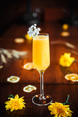 Side view of delicious sweet yellow alcohol cocktail in champagne glass on the wooden table with yellow flowers as decorative elements, vertical
