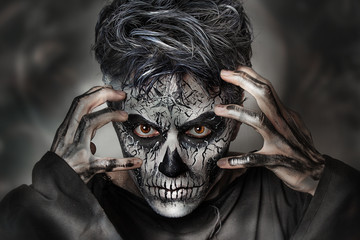 Close up studio portrait of man with skull face painting. Emotional beautiful guy. Professional Halloween makeup