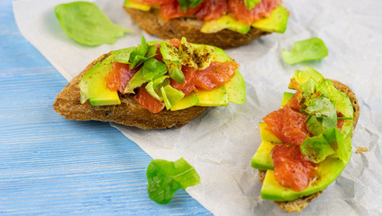 sandwiches of fresh avocado and red fish on a paper background, top view