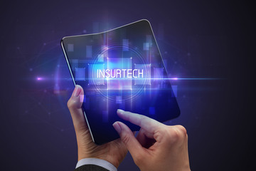 Obraz na płótnie Canvas Businessman holding a foldable smartphone with INSURTECH inscription, new technology concept