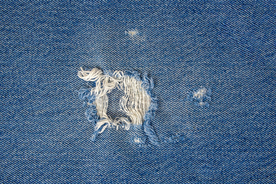 Close Up Of Frayed Hole In Blue Denim Fabric