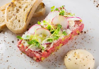 Beef tartare with toasts, radish and sauce on white plate
