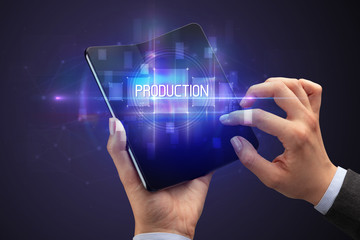 Businessman holding a foldable smartphone with PRODUCTION inscription, new technology concept