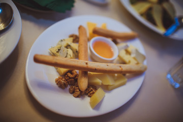 Cheese platter on a white plate with bread sticks and honey.