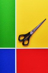 multi-colored paper background. Yellow, green, red and blue. On the yellow background lie scissors. Colorful pattern with white bands. abstract background