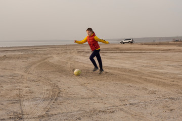 A boy of 10 years old plays soccer on an empty beach.