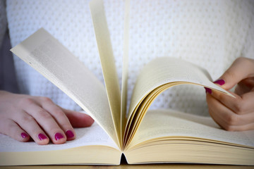 A young woman with a neat pink manicure sitting at table and browses in a book