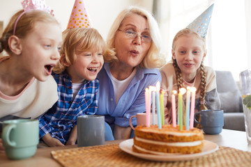 Grandmother blowing candles on the cake together with grandchildren during birthday party