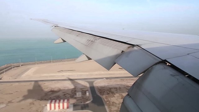 airplane wing on window view during plane landing on Hamad International Airport runway, Aerial shot at a low height of the sea and desert.