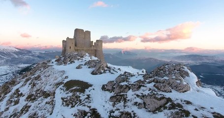 Aerial, drone shot towards the Rocca Calascio castle ruins on snowy Gran Sasso mountains, during sunset, in Abruzzo, Italy