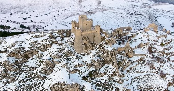 Aerial, orbit, drone shot around the Castello Rocca Calascio mountaintop fortress on snowy gran sasso mountains, dusk, in Abruzzo, Italy