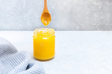 Indian desi ghee or clarified liquid butter in glass jar on neutral grey background