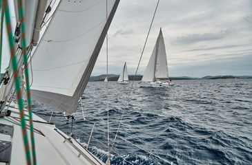 Naklejka premium Croatia, Adriatic Sea, 19 September 2019: The race of sailboats, the team sits on the edge of a boat board, bright colors, view of participants of race from other boat through ropes and sails