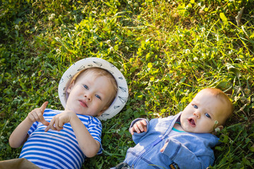 Happy european child and little brother lying on green grass background. Portrait of child boy and baby boy playing outdoor on lawn in garden. Freedom from ticks and insects