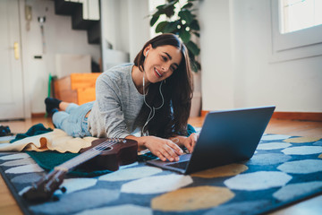 Happy young woman having online video call with family via laptop during home isolation lying on floor laughing, positive female teacher doing audio conference or webinar on computer device at home