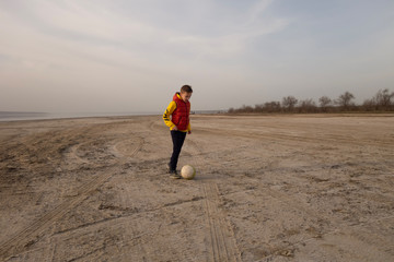 A boy of 10 years old plays soccer on an empty beach.