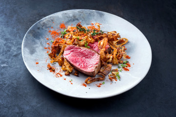 Barbecue dry aged beef fillet medallion steak natural with fried onion rings and carrots as closeup on a modern design plate with copy space