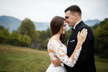 Stylish groom kissing gorgeous bride in sunset light, perfect moment, wedding couple, luxury ceremony at mountains with amazing view