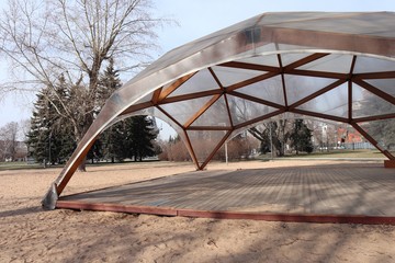 Wooden modular building in the form of a dome. The tent stands on the sand in the center of the city park.