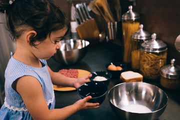 little girl while preparing meatballs in the kitchen during the quarantine
