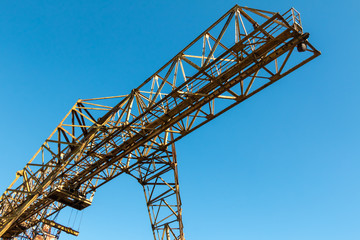 Vintage working gantry crane rusty yellow, bottom view, close-up against a blue spring sky