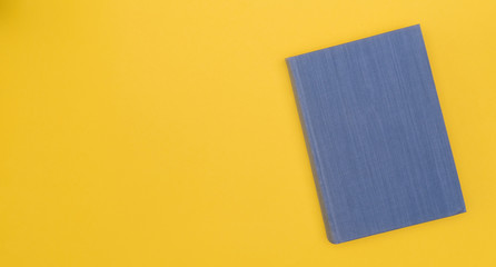Blue book with blank cover on a yellow background. Hard cover. Top view. Copy space