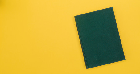 Green book with blank cover on a yellow background. Hard cover. Top view. Copy space