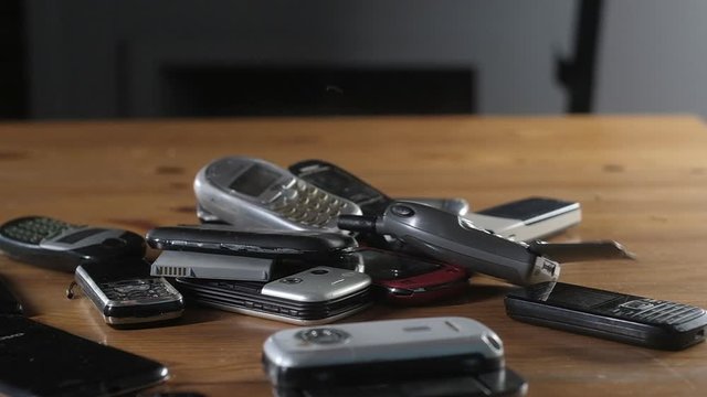 outdated mobile phones fall on table and break. Old broken scratched dusty cell phones lie in pile. Analog communication in office. Modern wireless technology. Close-up of old outdated mobile phone