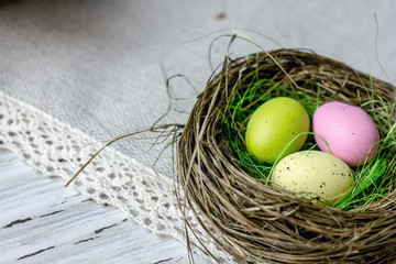 Three easter eggs of yellow green pink in a nest on a light wooden table, mine space, flat lay, top view. Easter Greeting Card