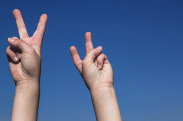 Children's hands showing peace victory sign. Both hands raised on the clear blue sky. Gradient background, copy empty space for text, body parts concept.