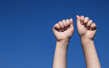Children's fists raised up showing power. Kid's hands raised against the clear blue sky, symbol of resistance movement. Body parts concept, close up, gradient background, copy empty space for text.