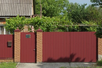 red metal gate and closed door on a rural street on a sunny day