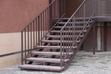 brown iron staircase with wooden steps on the street against a  wall
