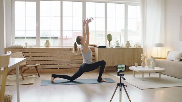 Attractive Caucasian female recording making live stream or vlog about doing yoga at home. Stay home, quarantine workout. Shot on ARRI Alexa Mini with Cooke S4 lenses