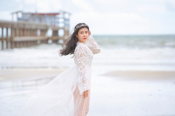 Fototapeta na wymiar Beautiful woman in white dress happily strolling at the beach, beautiful woman dressed in white bride