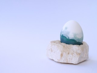 Blue, green, turquoise and white homemade easter egg isolated colored with a red cabbage natural colour on a white background with blank space on a stone pedestal closeup.