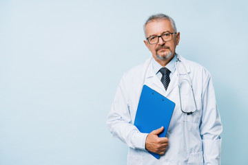 Elderly bearded male doctor in white uniform with a stethoscope with a blue folder. Doctor on the background of a medical research laboratory.