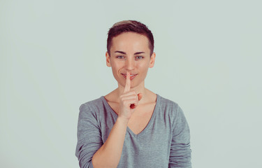 Closeup portrait happy young woman placing finger on lips asking shhhhh, quiet, silence isolated on green gray wall background. Human face expressions, signs emotions, feelings, body language reaction