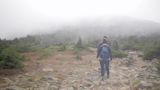 A young active hiker couple walks along a mountain summit trail and disappears into thick cloud smoke.