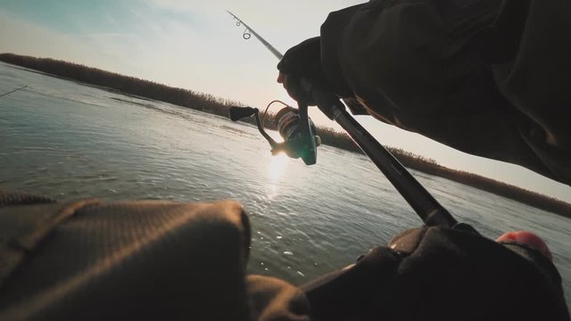 An angler spinning predatory fish from a boat on the beautiful river at sunset