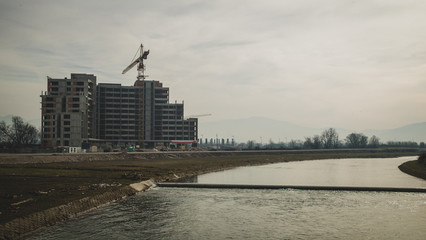 A hotel next to a river is seen under construction. Giant crane just next to the construction