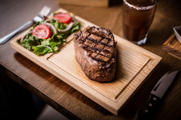 Thick grilled juicy beef steak on a wooden cutting board, salad and wine, Reb eye, Angus 