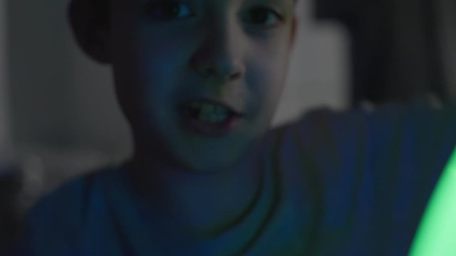 Boy plays with glow green stick in bed at night. Close-up face