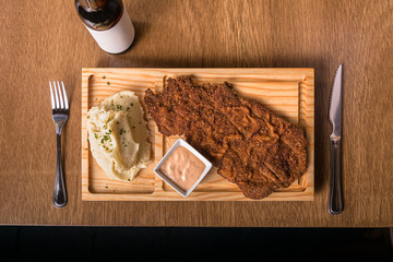 breaded beef, Milanese fillet whit mashed potatoes served on a wooden cutting board whit bottle of dark beer, zenith